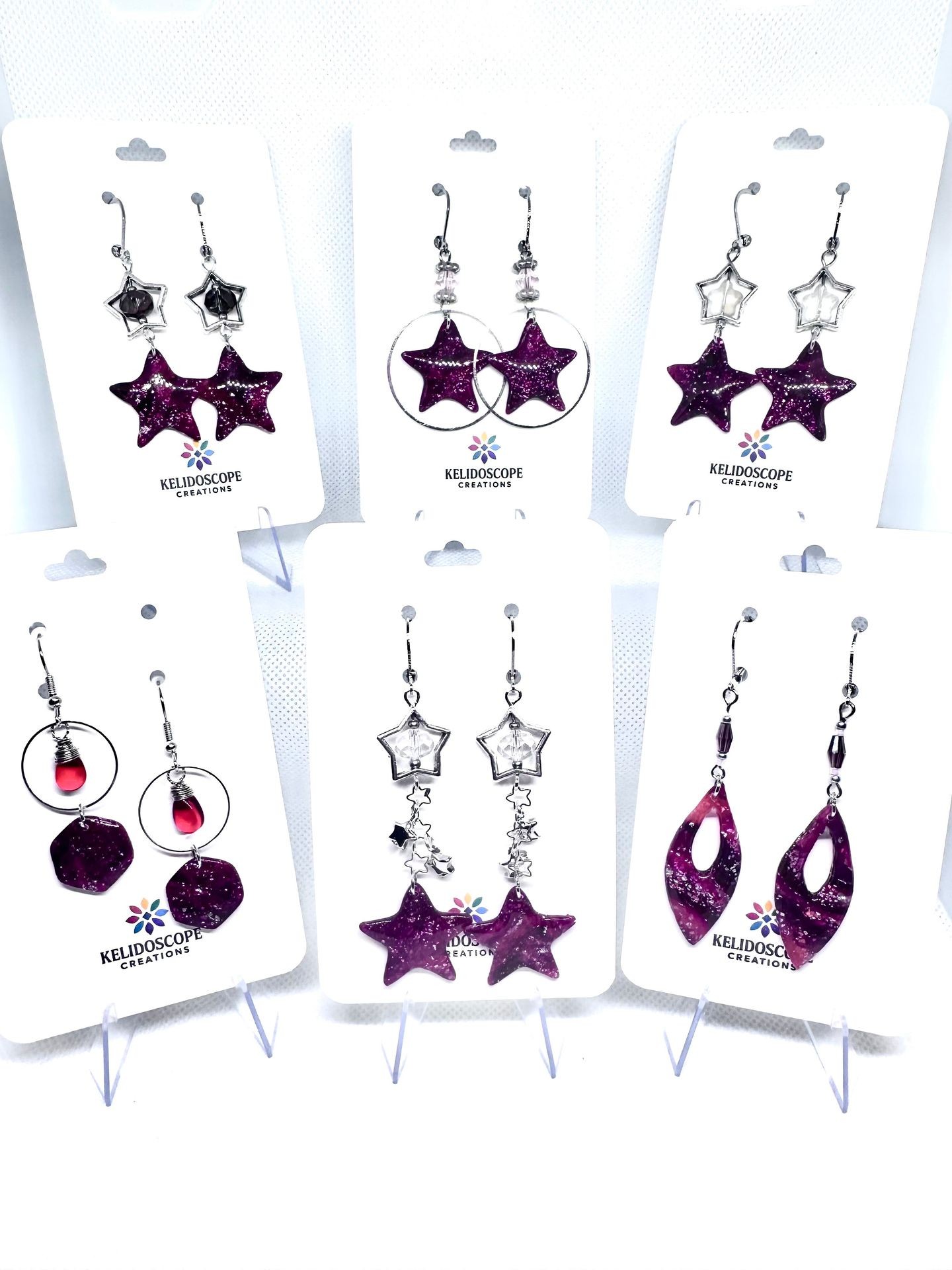 Display of various star-themed earrings with purple and silver accents on white cards.