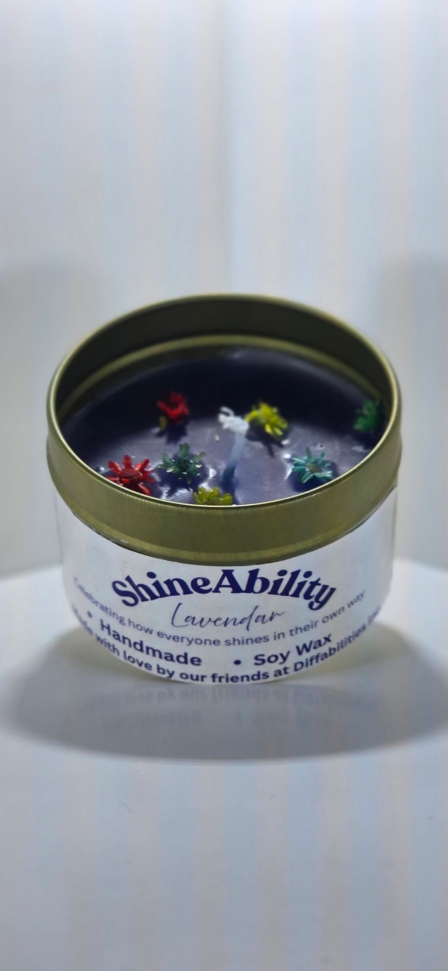 ShineAbility lavender handmade soy wax candle in a tin container, with colorful decorations on top.