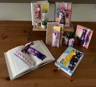Books displayed on a table with colorful bookmarks, plants, and pens in holders.