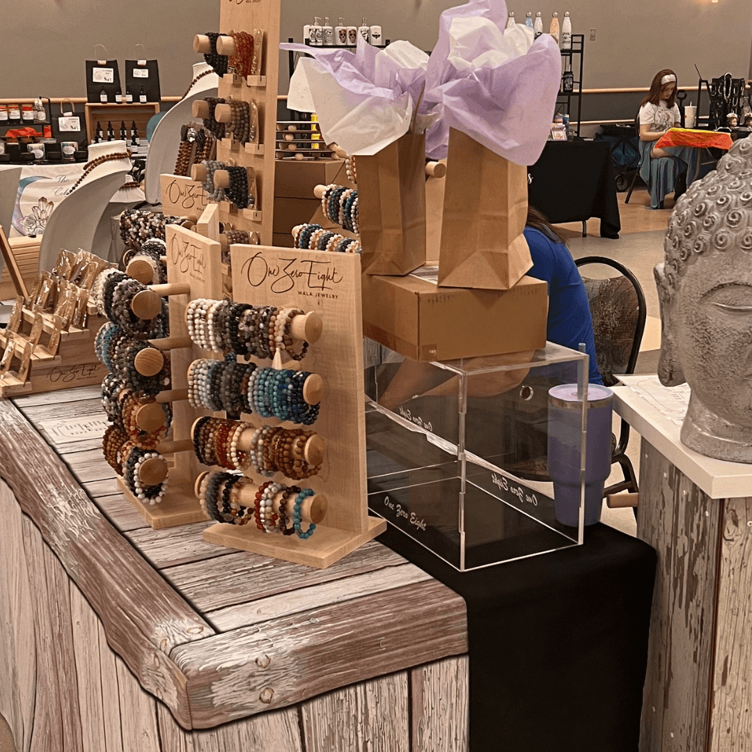 Craft fair booth displaying beaded bracelets on wooden stands and decorative gift bags.
