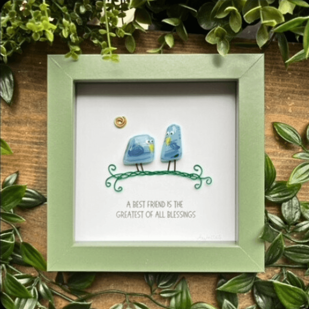 Framed art with two birds and a quote about friendship, surrounded by lush green leaves.
