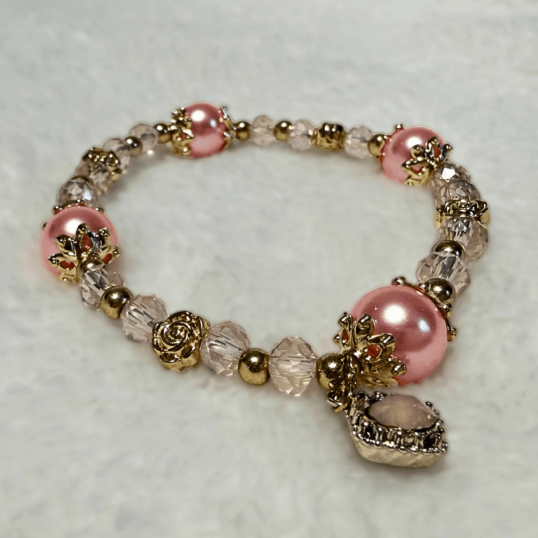 Elegant bracelet with pink pearls, gold accents, and a dangling gemstone charm on a textured surface.