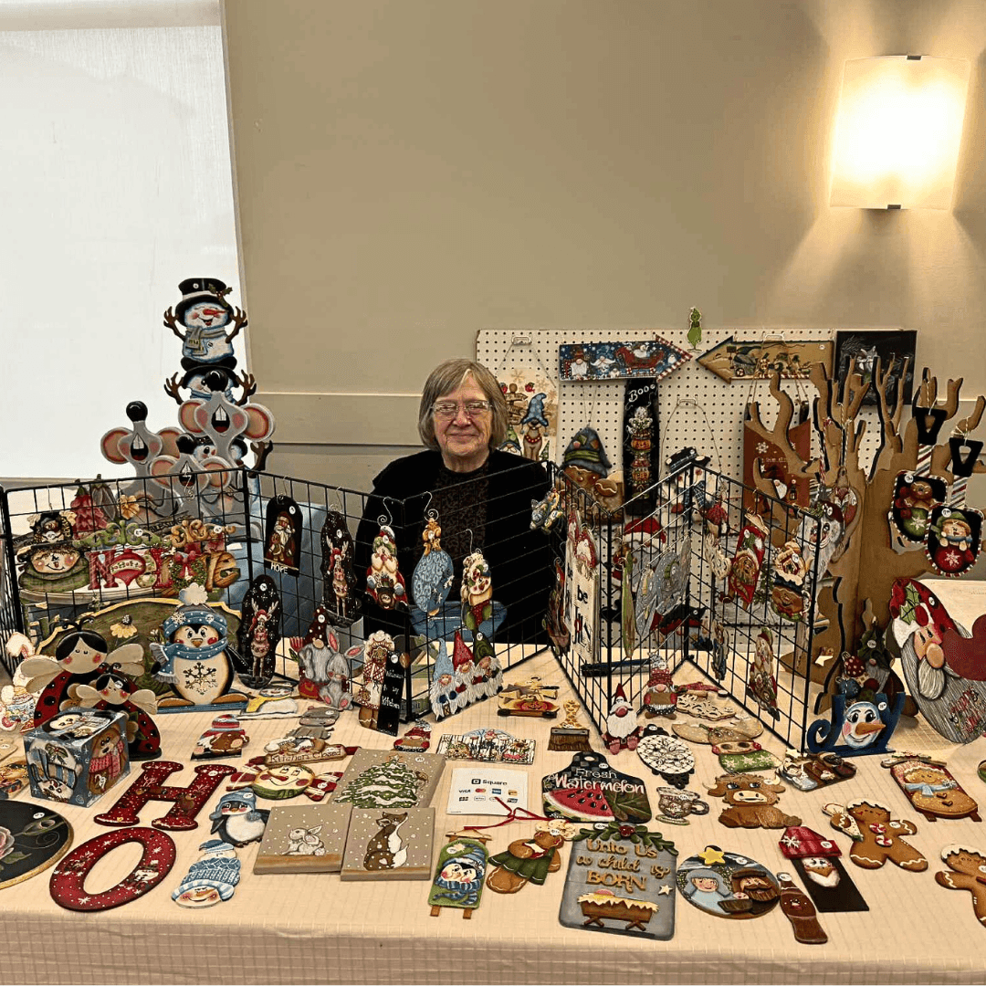 Booth display of various handcrafted Christmas ornaments, decorations, and festive items arranged on a table.