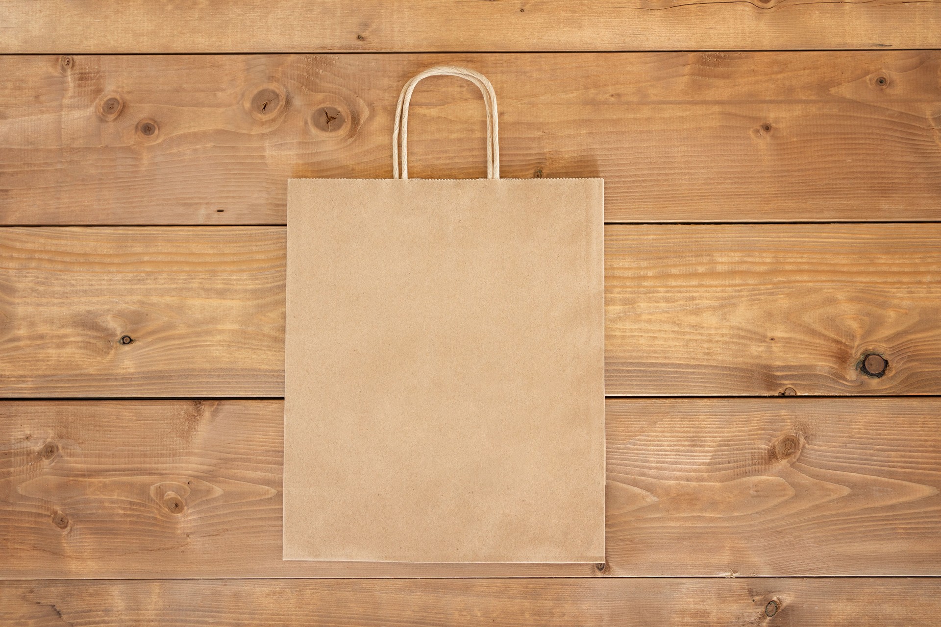 Brown paper craft bag on wooden background. Centre composition with empty spot for text. Responsive design mockup. Flat lay